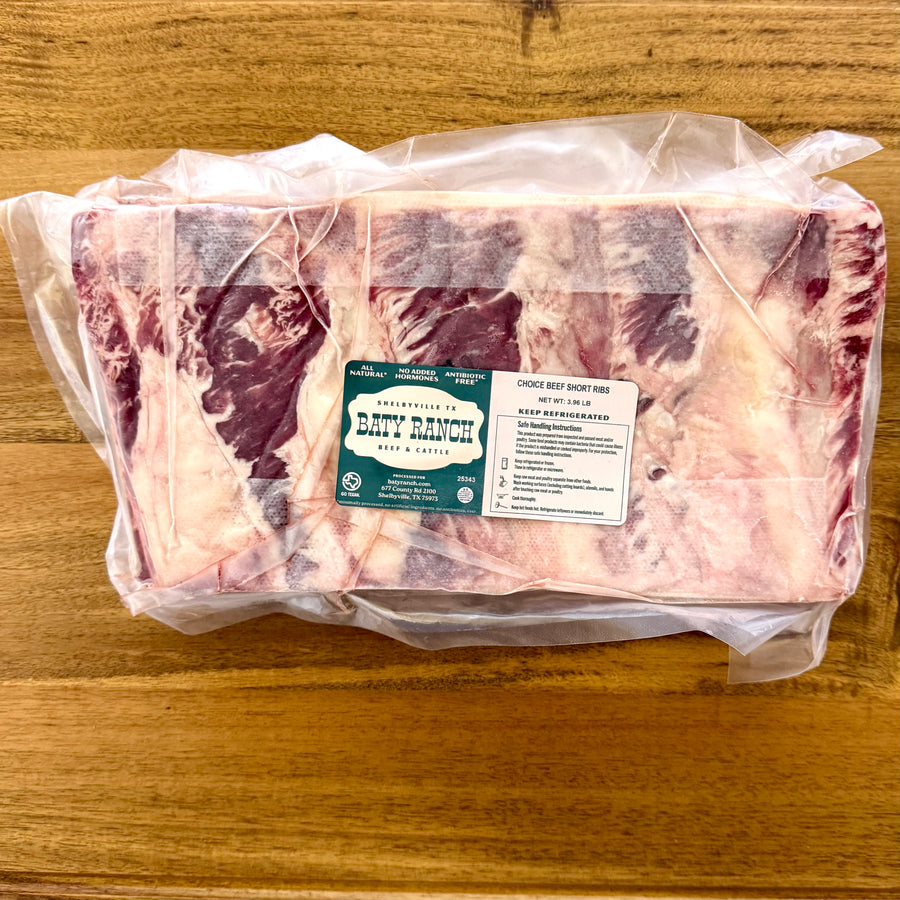 Packaged raw beef short ribs with a label on a wooden surface