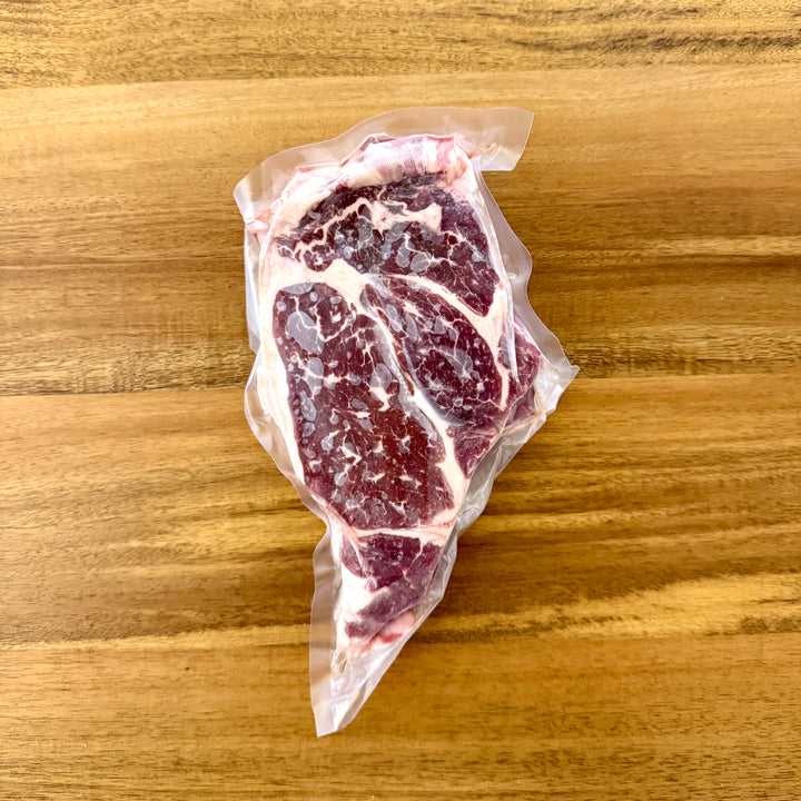Raw steak wrapped in plastic on a wooden surface