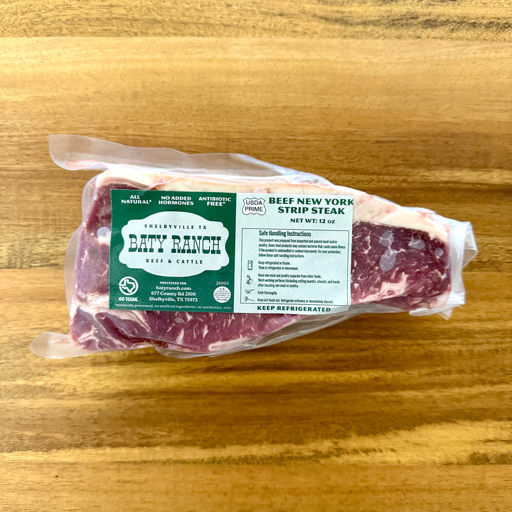 Packaged beef New York strip steak with Baty Ranch label on a wooden surface