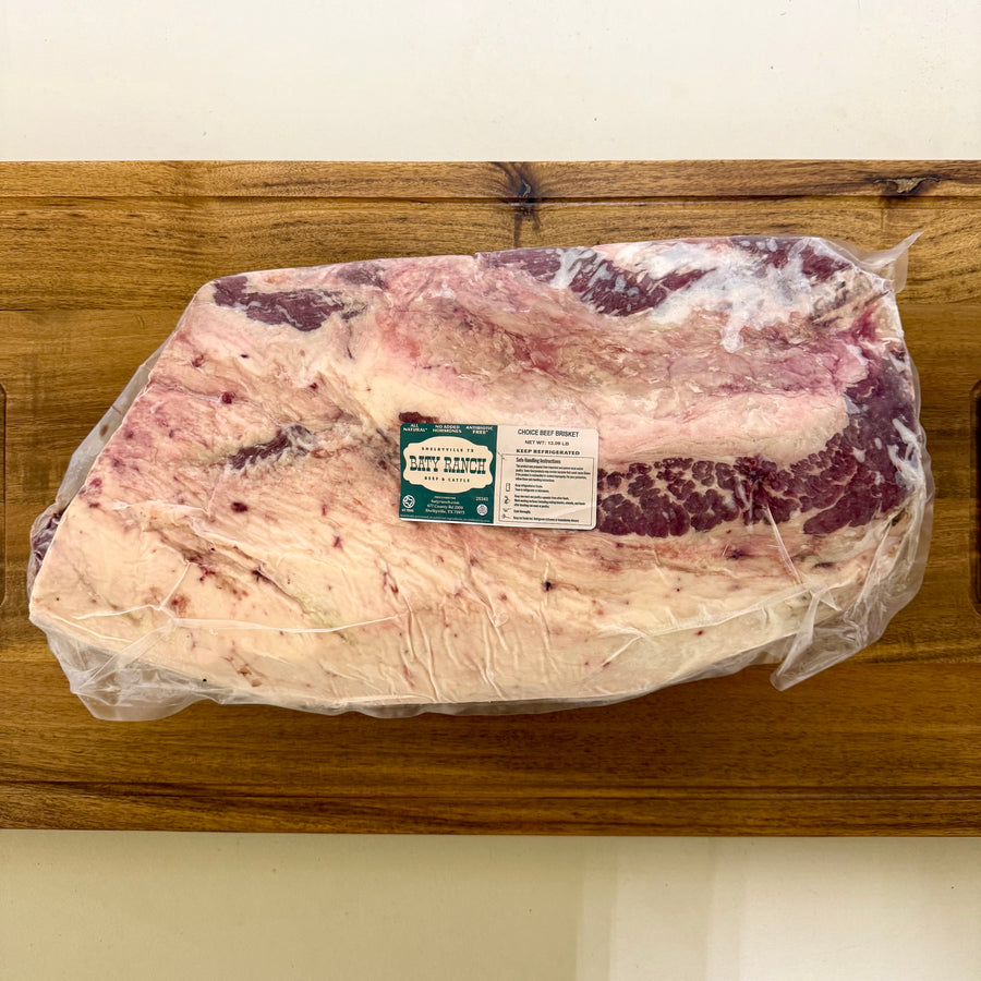 Packaged raw beef brisket on a wooden cutting board with a label.