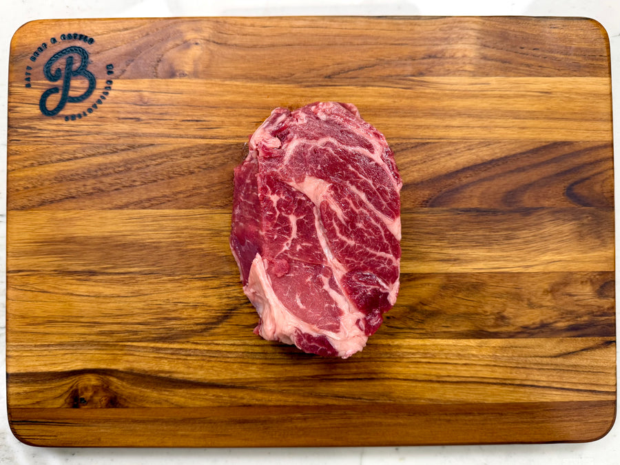 Raw steak on a wooden cutting board with a brand logo.