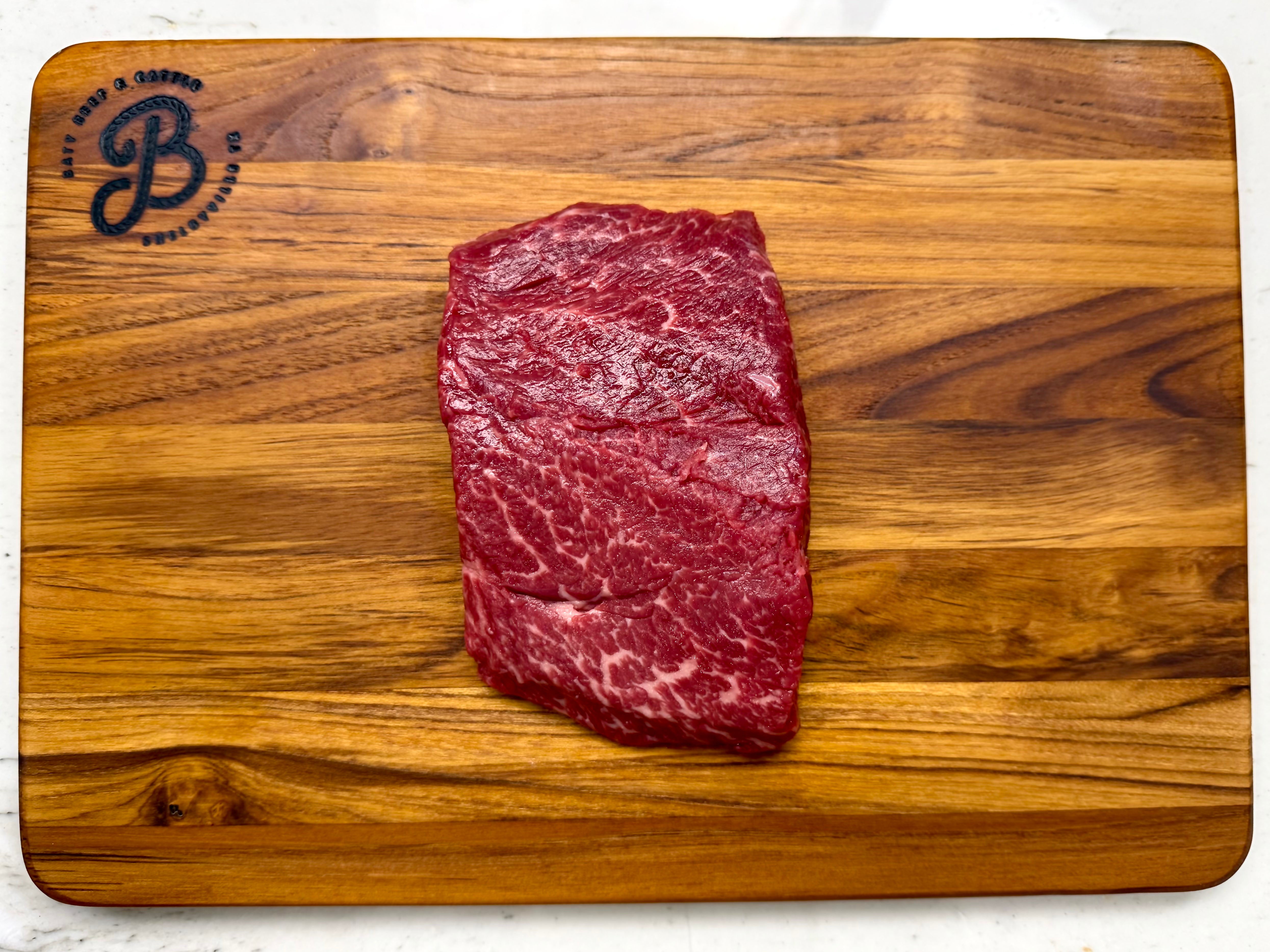 Raw Denver steak on a wooden cutting board with a brand logo.
