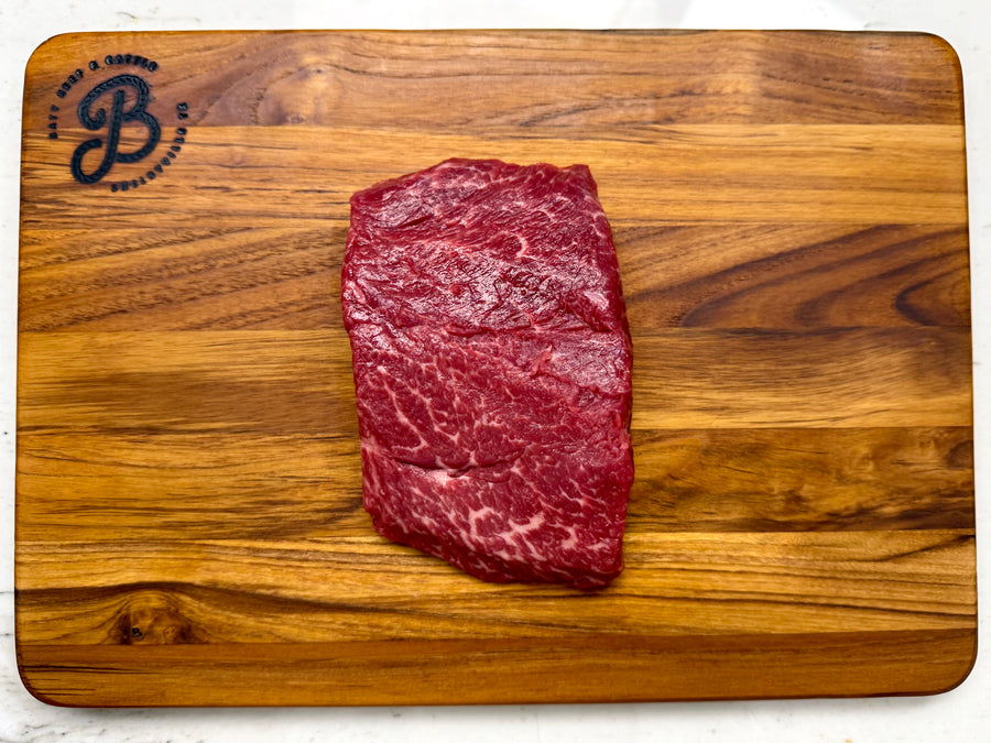 Raw Denver steak on a wooden cutting board with a brand logo.