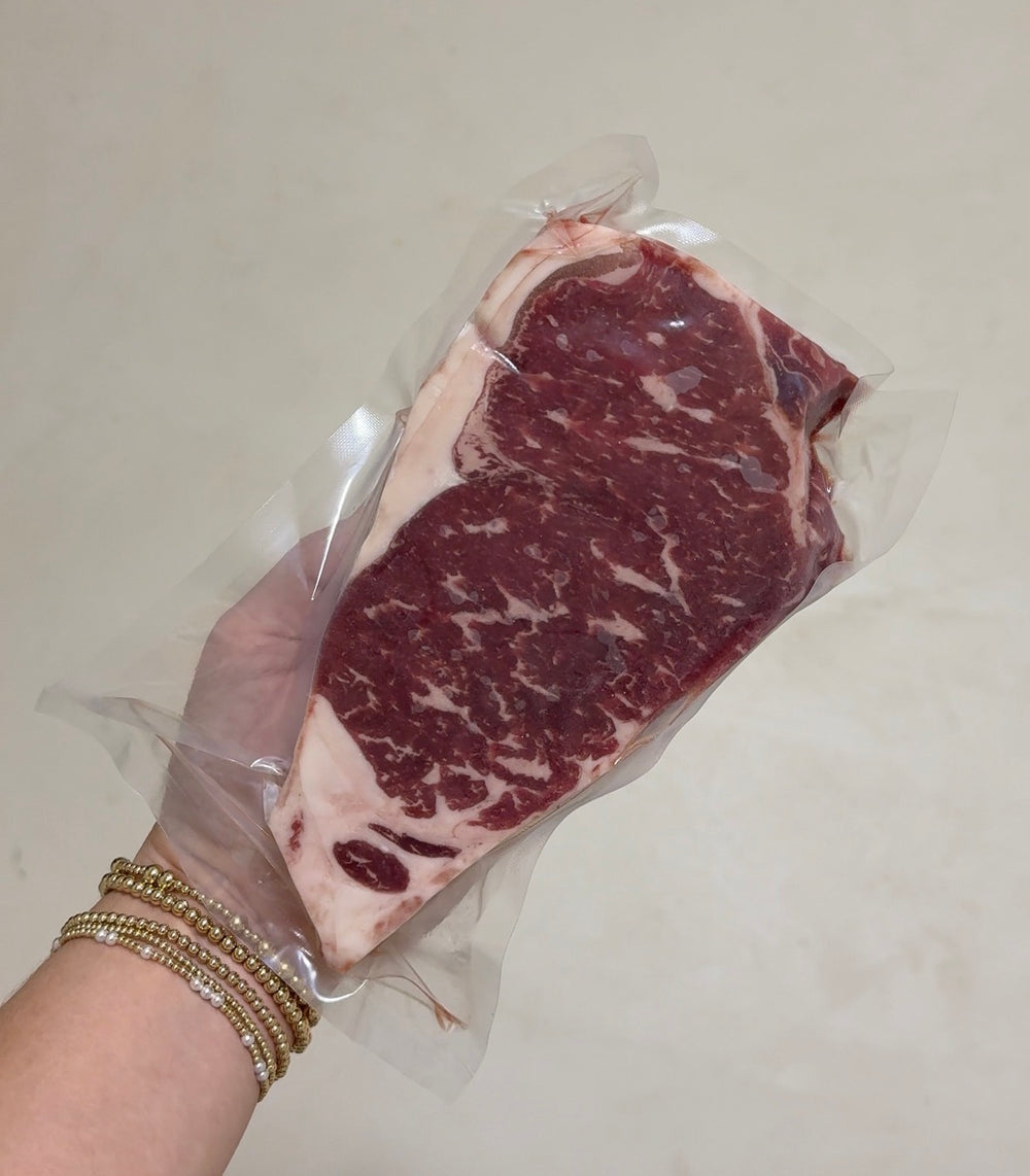 Hand holding a package of raw steak with a plain background