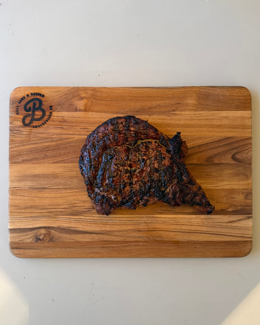 Grilled steak on a wooden cutting board with a brand logo.