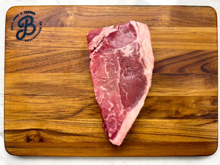 Raw new york strip steak on a wooden cutting board with a brand logo.