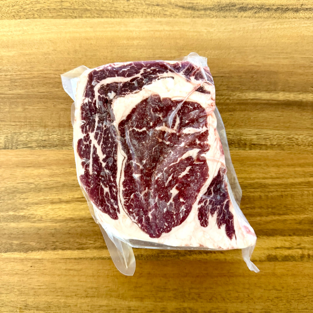Raw ribeye steak vacuum packaged on a wooden surface.