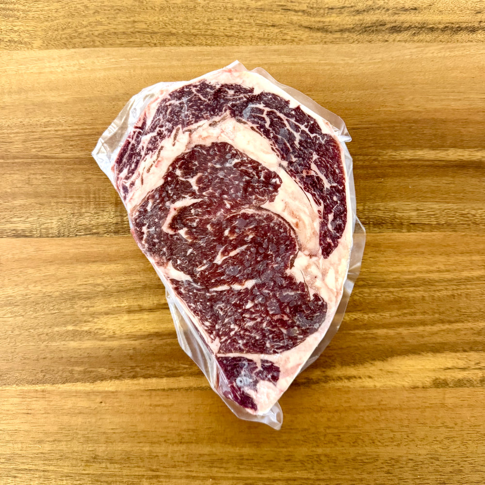 Raw ribeye steak vacuum packaged on a wooden surface.